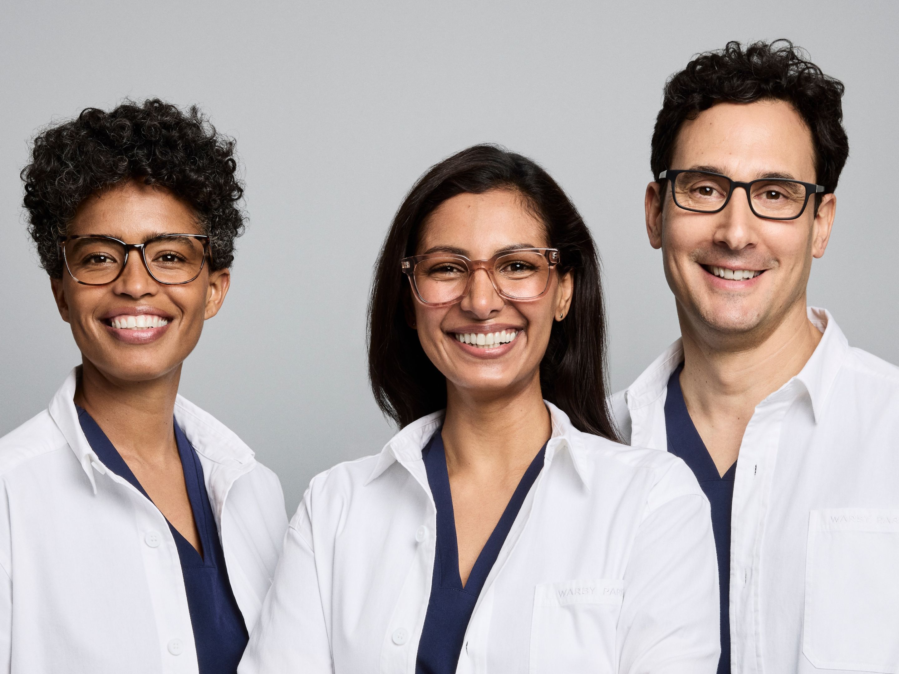 Optometrists wearing glasses and smiling at the camera.