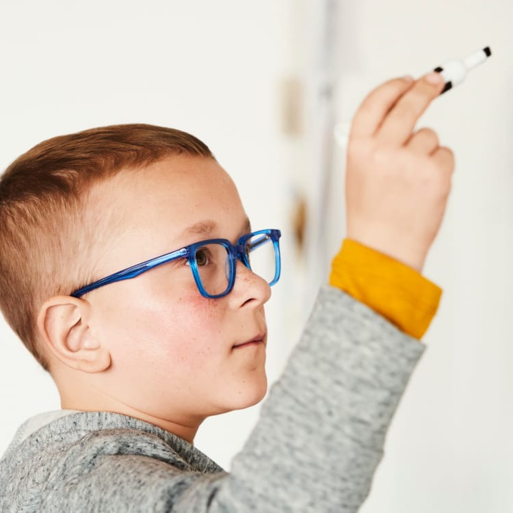 Child with a marker wearing glasses writing into a board.