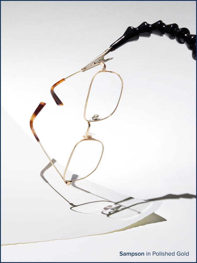 Eyeglasses holder by a tool hanging on top of a piece of papel.