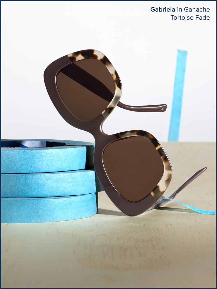 Sunglasses leaning towards blue tapes in a brown table.
