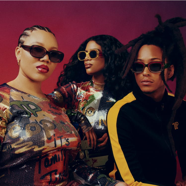Three people wearing stylish sunglasses and colorful outfits, posing confidently against a dark red background.