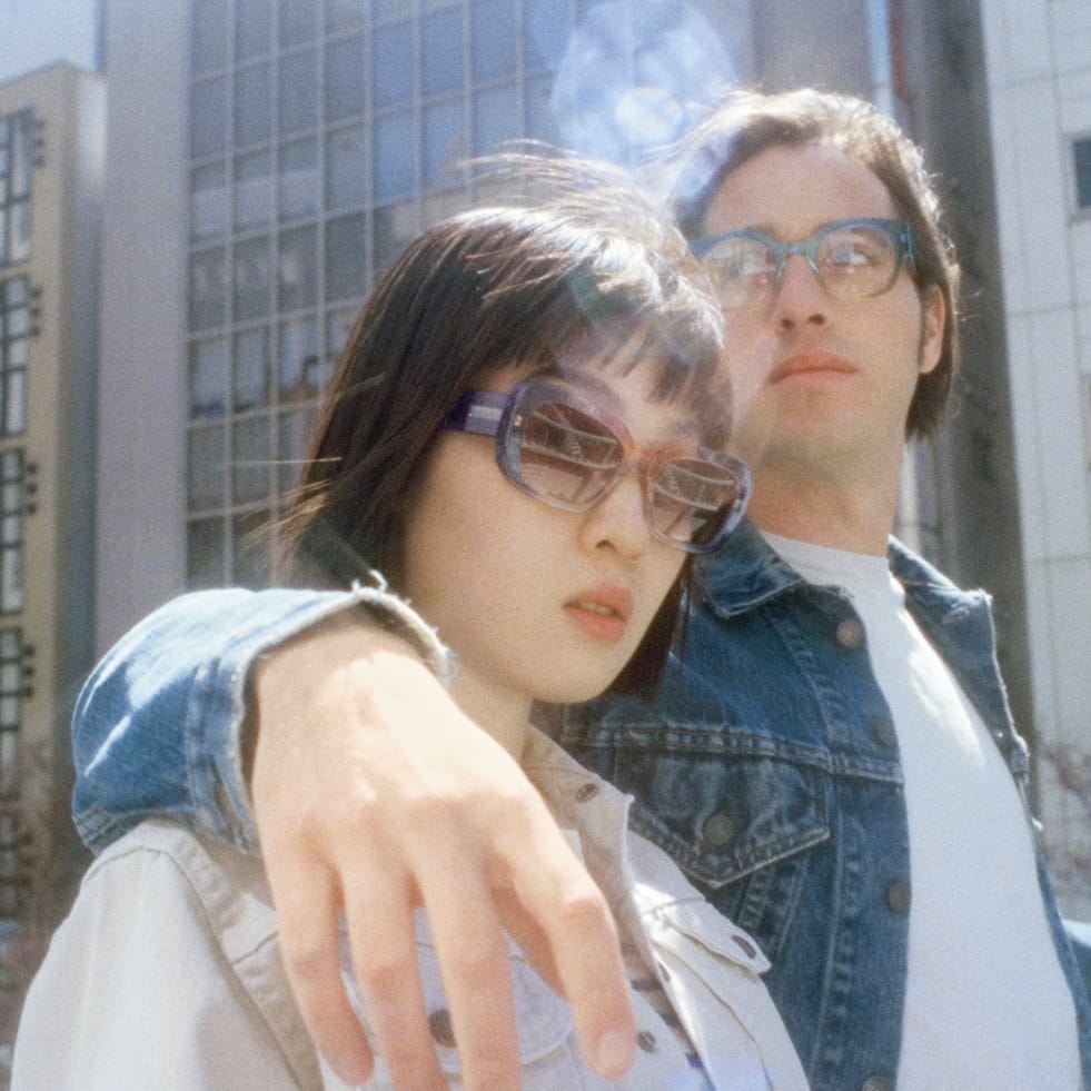 Model on the left wears the Bridie frame in Hyacinth Crystal Fade; model on the right wears the Rocco frame in Coastline Crystal Fade