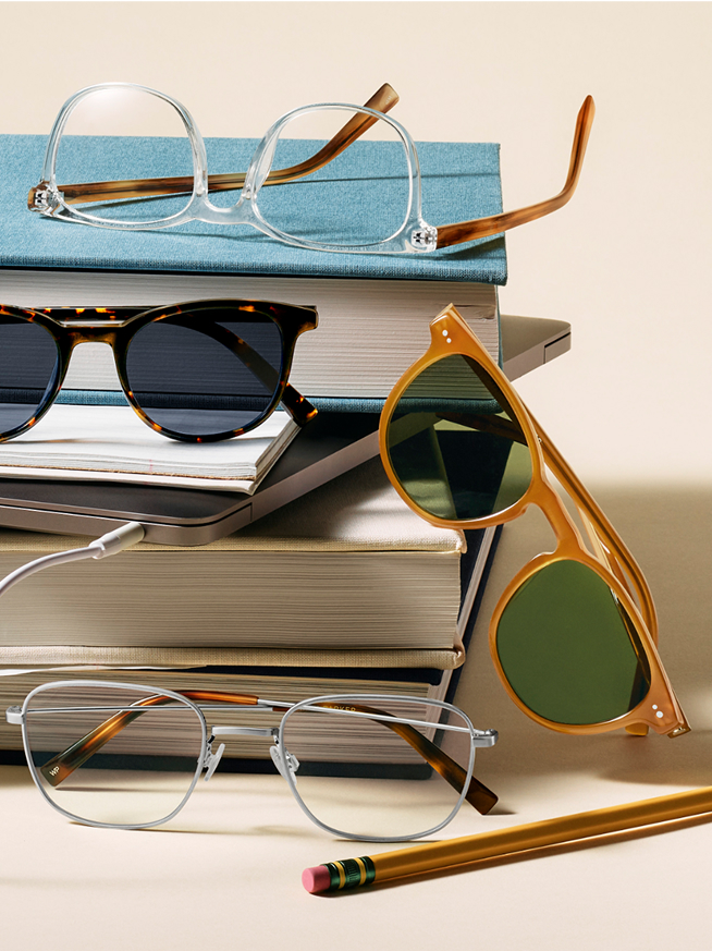 Four pairs of eyeglasses and sunglasses on fabric next to a brown leather bag and case.
