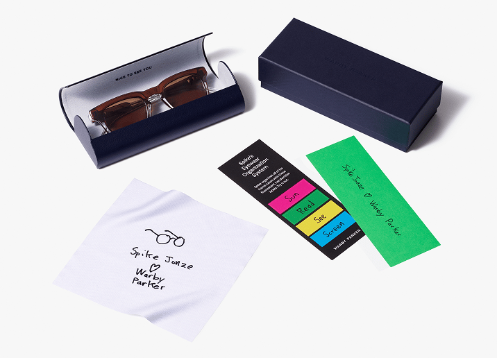 A pair of brown sunglasses in a blue case and a blue box. Accessories include a cleaning cloth and two green and black cards.