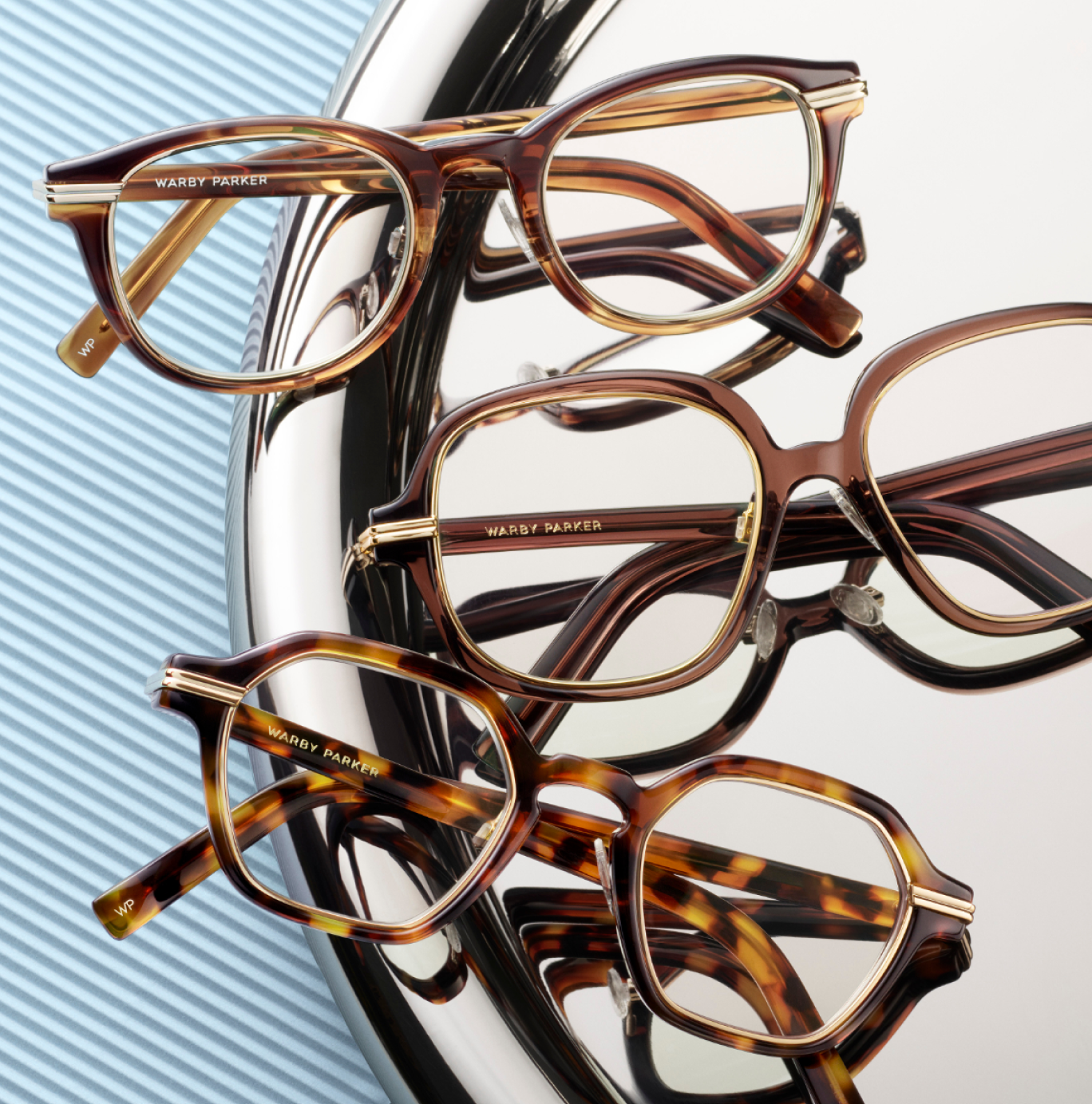Three pairs of stylish eyeglasses with tortoise shell frames are displayed on a silver tray.