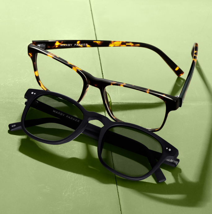 A pair of black eyeglasses with tortoise shell temples rests atop a pair of black sunglasses.