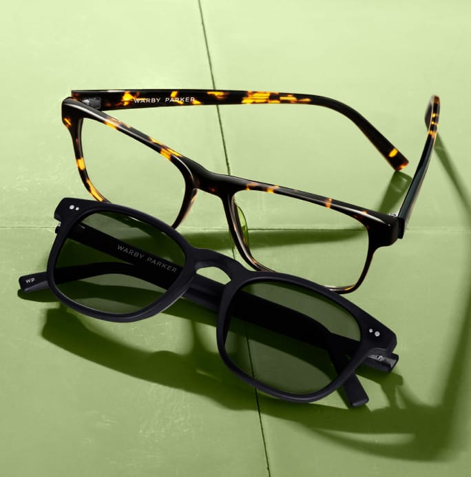 A pair of black eyeglasses with tortoise shell temples rests atop a pair of black sunglasses.