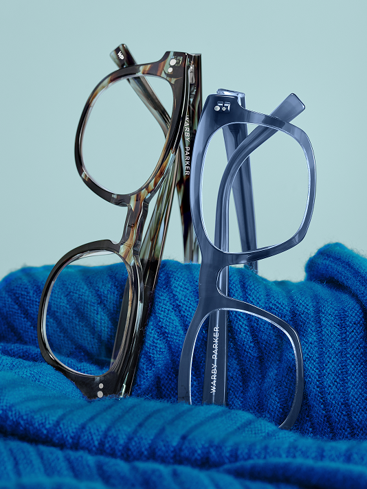 Two pairs of eyeglasses, one tortoiseshell and one navy, rest on a bright blue scarf.