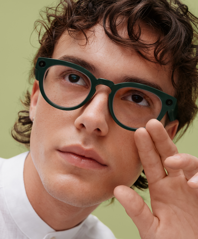 Man with curly hair and green glasses touches his face.