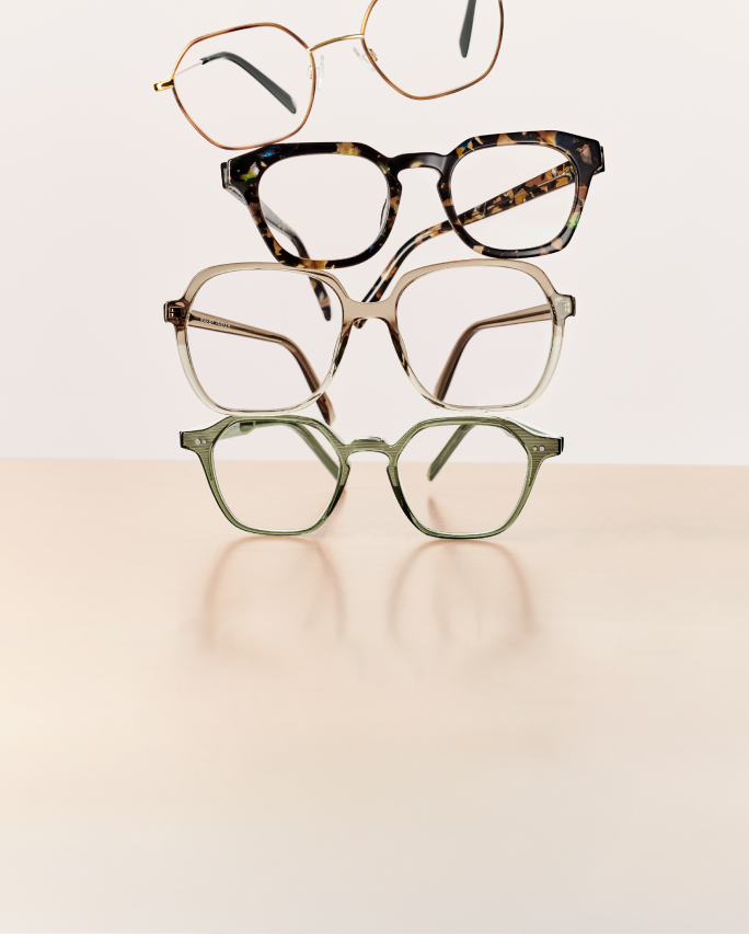 Four pairs of eyeglasses stacked on a beige surface with a light background.
