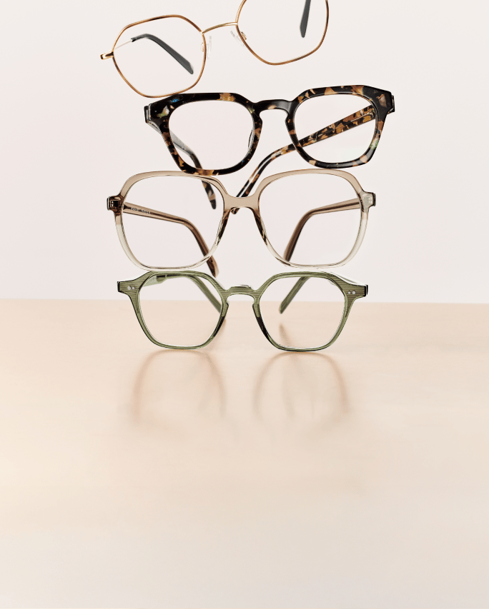 Four pairs of eyeglasses stacked on a beige surface with a light background.