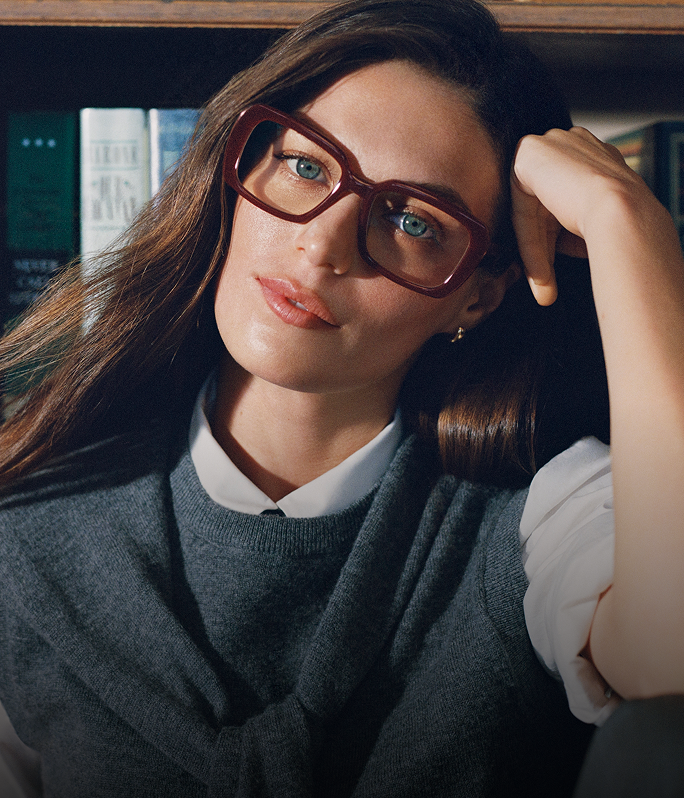 Two pairs of Warby Parker eyeglasses, one tortoiseshell and one green, placed on lined notebook paper with a red pen and pencil shavings.
