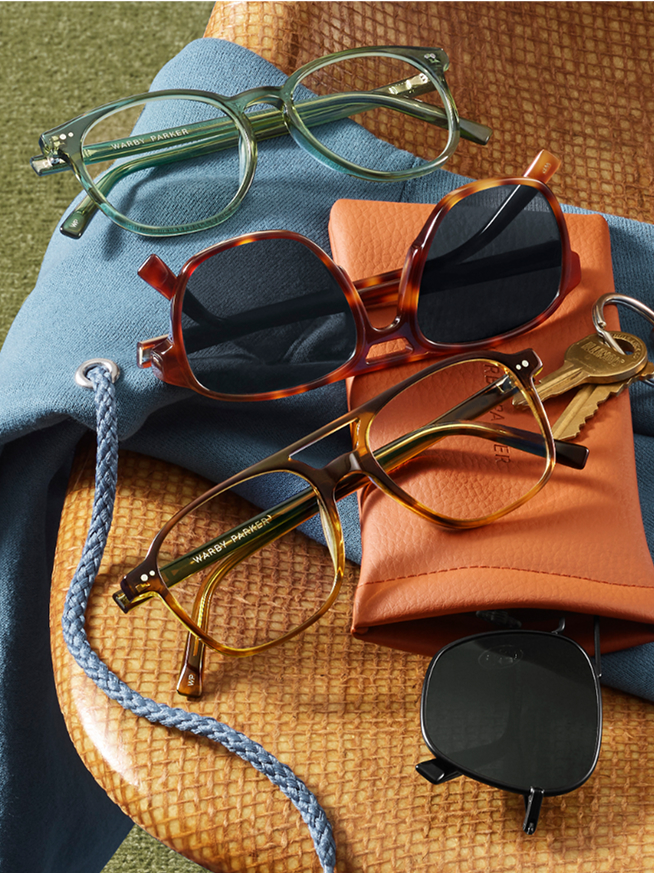 Four pairs of eyeglasses and sunglasses on fabric next to a brown leather bag and case.