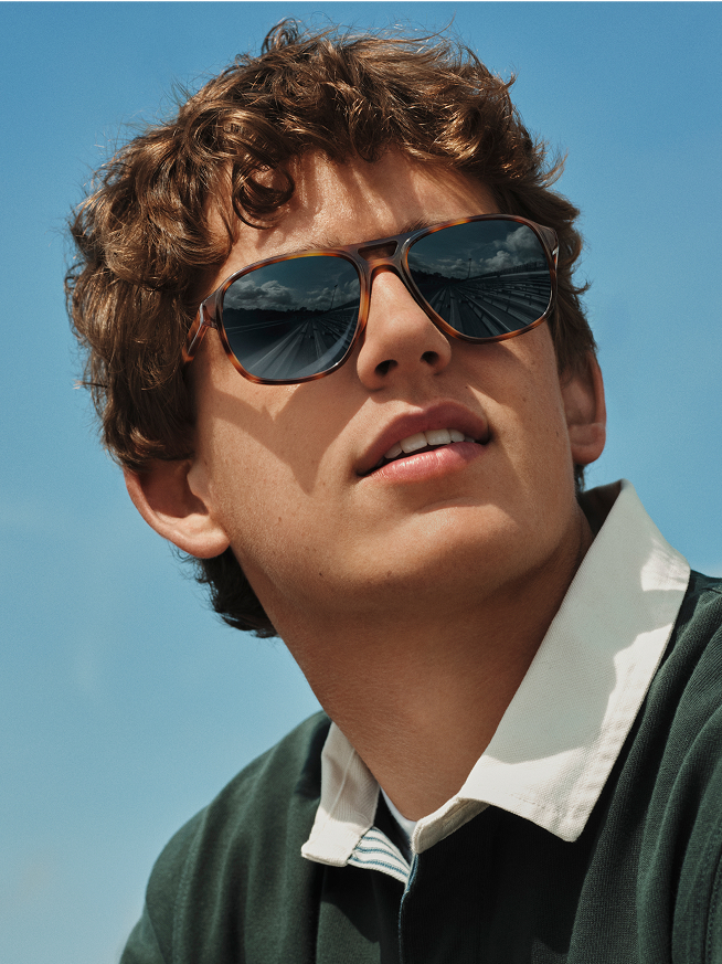 Close-up of a young man with curly hair and tortoiseshell sunglasses looking right.
