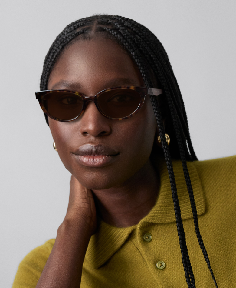Close-up of a dark-skinned woman wearing tortoiseshell cat-eye sunglasses and a green sweater.
