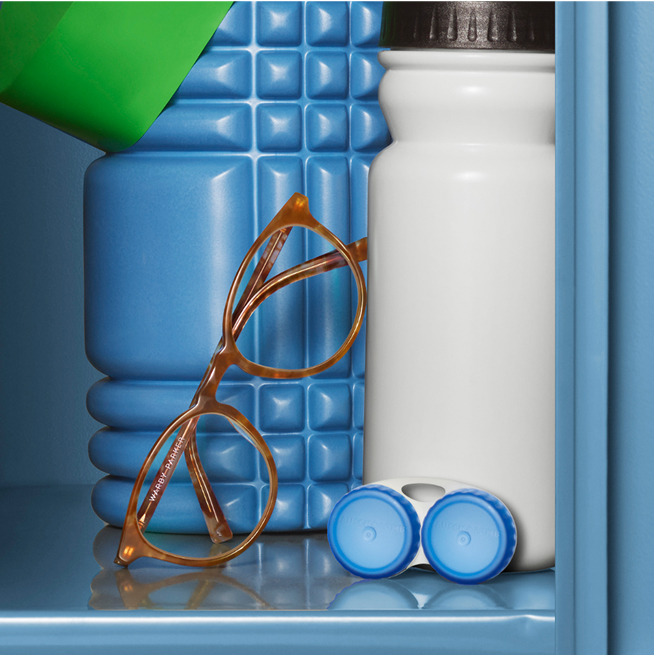 Tortoiseshell glasses leaning against a blue foam roller, next to a white water bottle and blue contact lens case.