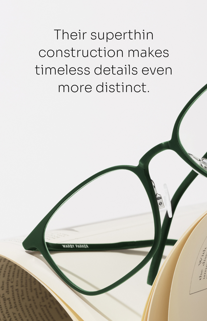 A pair of thin, green-framed glasses rest on an open book.