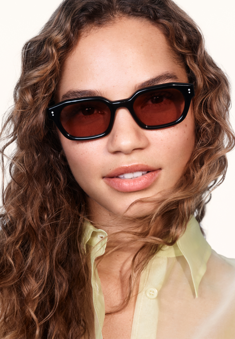 Black Warby Parker eyeglasses rest on top of three books with colorful spines.