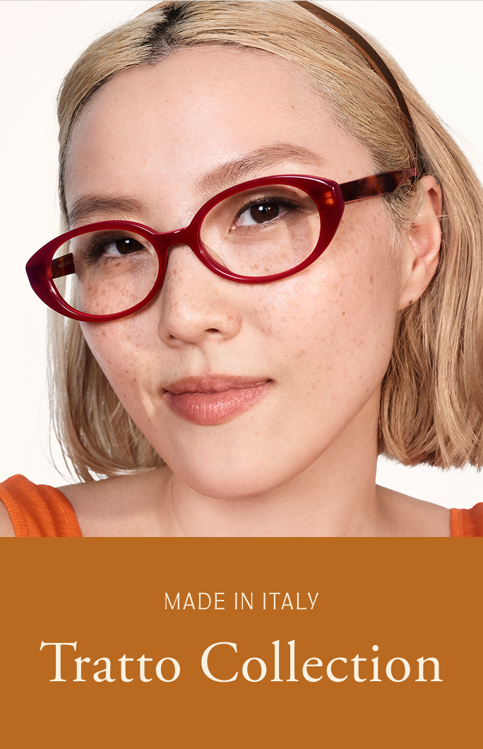 A young woman with blonde hair wears red oval-shaped glasses and smiles gently.