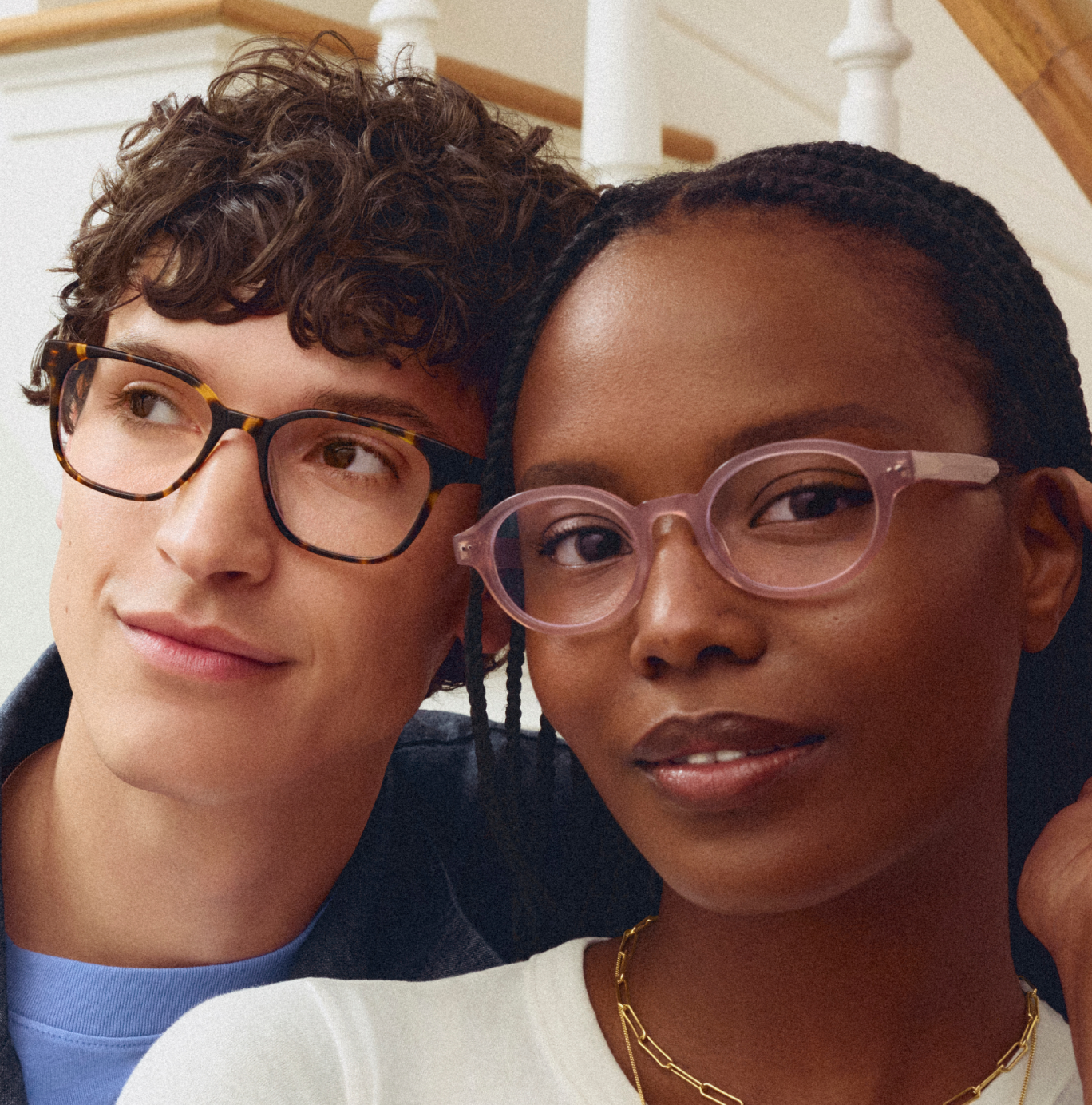 A young man and woman wearing glasses. The man has brown hair and glasses with tortoiseshell frames. The woman has dark skin, dark hair, and light pink glasses.