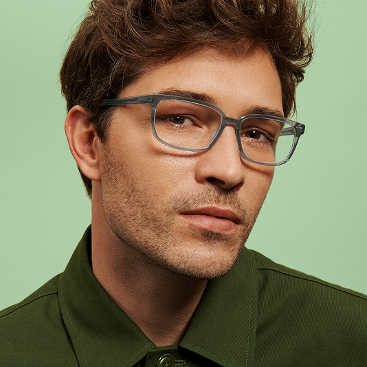 A man wearing eyeglasses with a dark green shirt against a light green background.