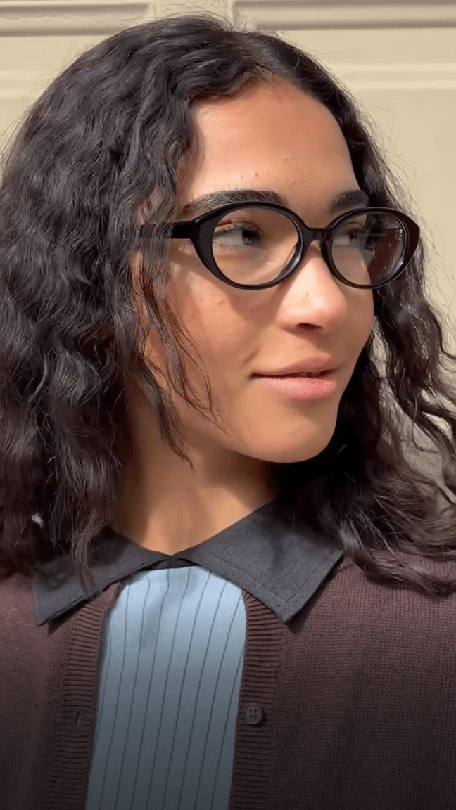 Close up of a woman wearing glasses, looking to the side with a smile.