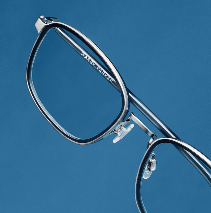 Close-up of eyeglasses with silver frames and clear lenses against a blue background.