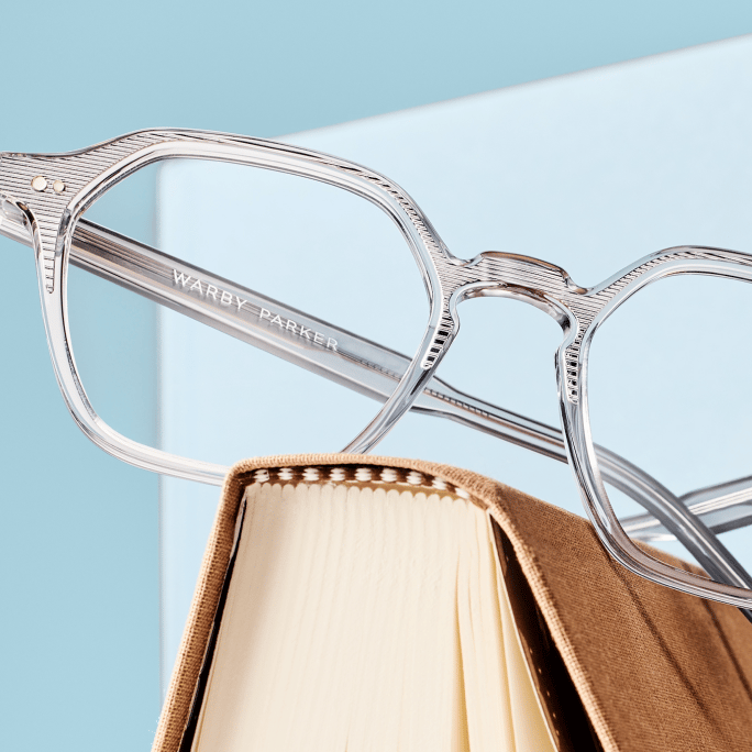 Clear Warby Parker glasses resting on the top edge of a brown hardcover book.
