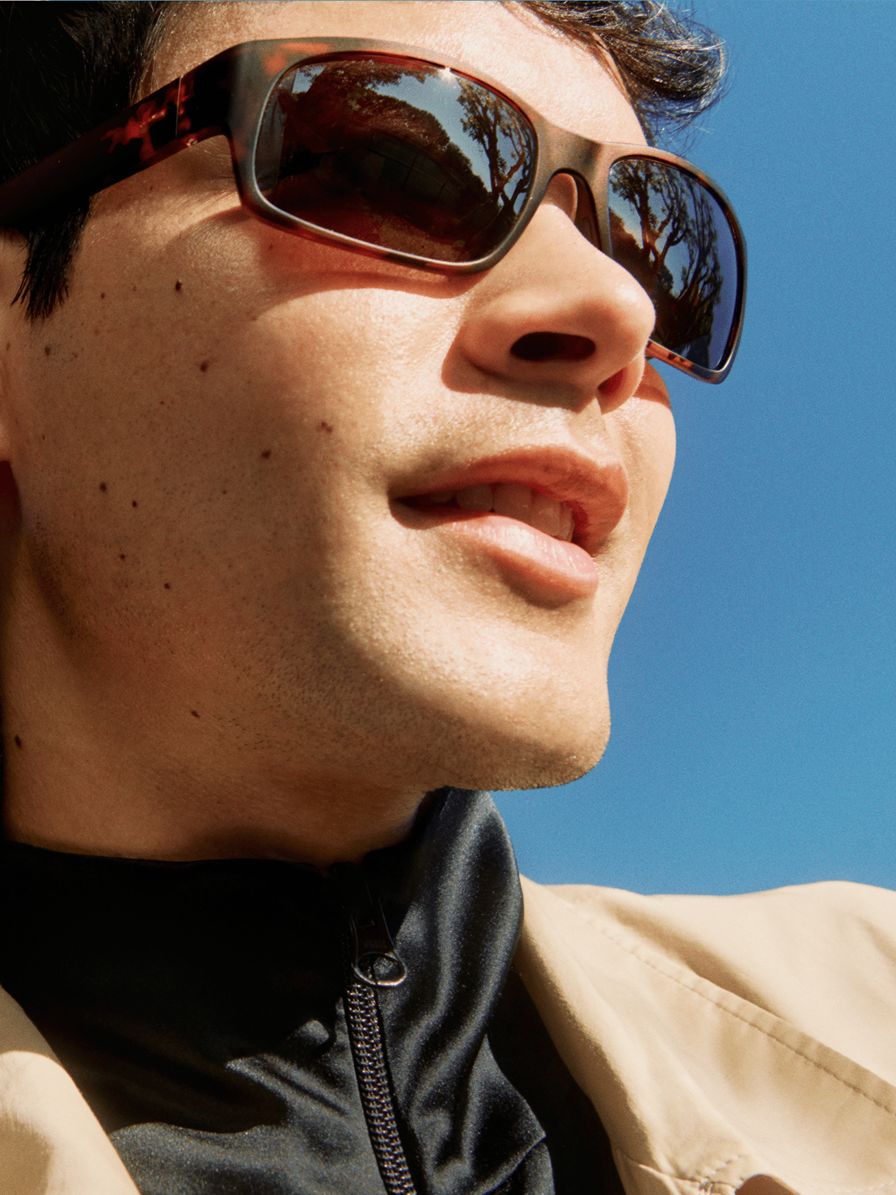 A man with sunglasses looks to the side against a bright blue sky.