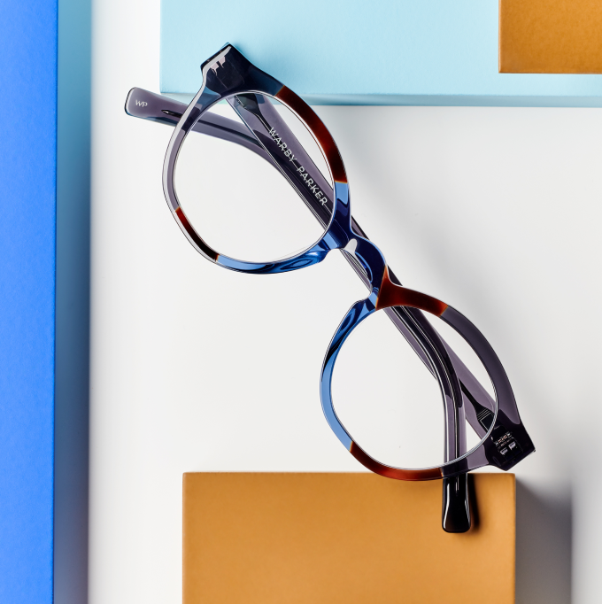 Tortoiseshell eyeglasses resting on a white surface with blue and orange blocks.