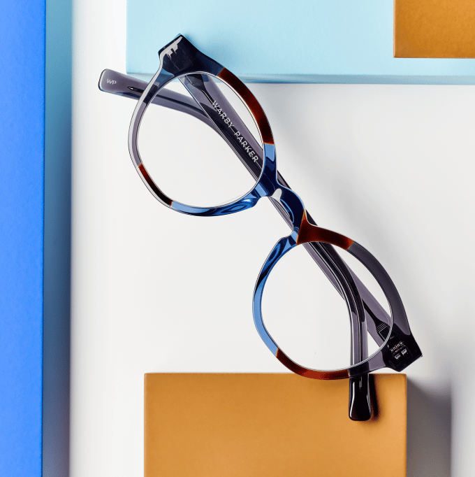 Tortoiseshell eyeglasses resting on a white surface with blue and orange blocks.
