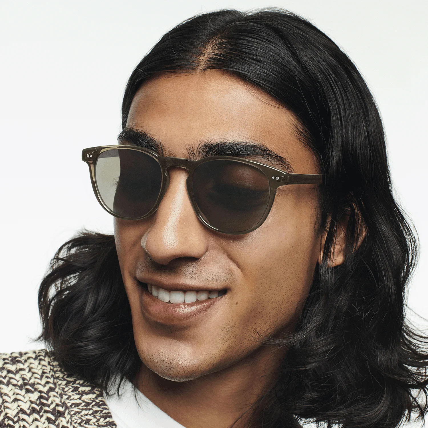 Person with long hair wearing sunglasses, smiling, and looking down.