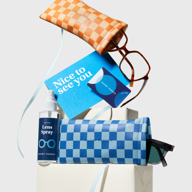 Collection of eyewear accessories including orange and blue checkered cases, lens spray, a blue greeting card with "Nice to see you," and a Warby Parker gift card, arranged with sunglasses and a ribbon.