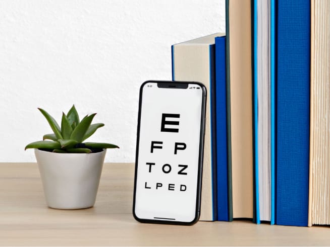 Virtual Vision Test displayed on a smartphone with a plant and blue books behind on top of a table.