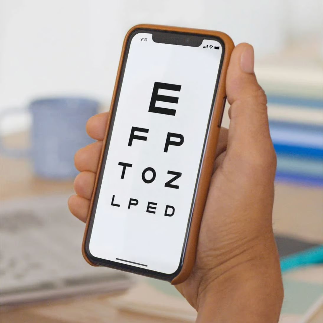 Hand holding a phone displaying eye exam chart.