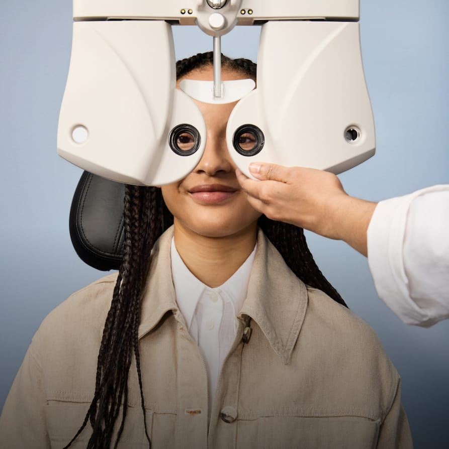 Person having their eyes examined with a phoropter by an optometrist against a blue background.