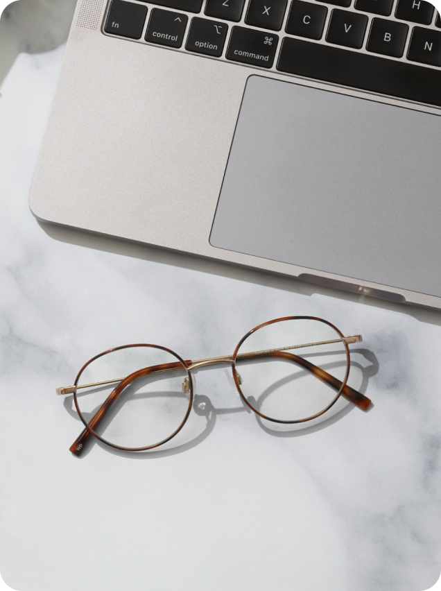 Round glasses with tortoiseshell frames next to a laptop on a marble surface.