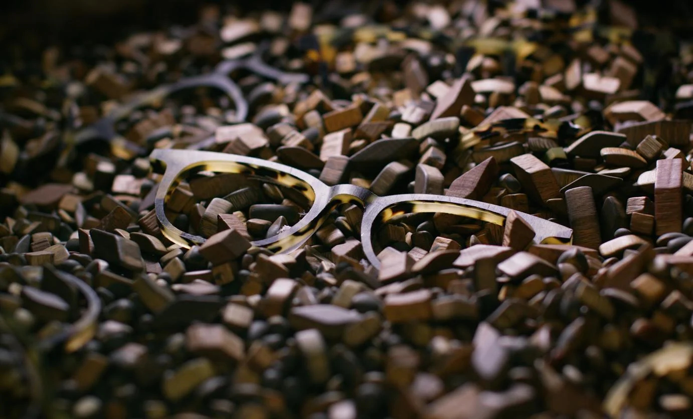 Large pile of wood chips with matted acetate frame faces mixed in in a dark space with a light indirectly shining on the frame. 