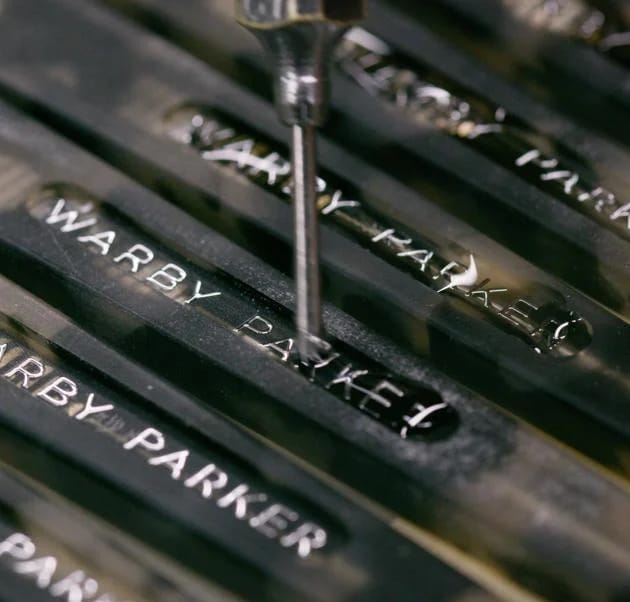 Warby Parker Logo being screwed into frame arm with small screw driver carefully applied by hand