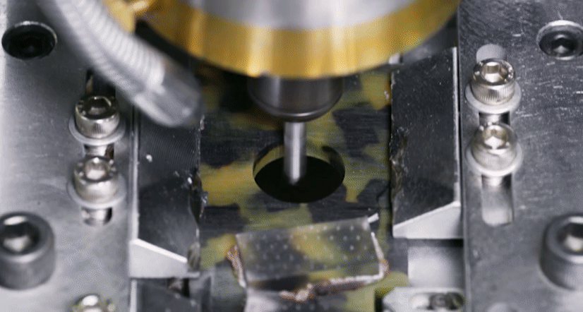Looping video of a metal machine cutting out frame shape from a sheet of acetate of yellow and black tortoise coloring.