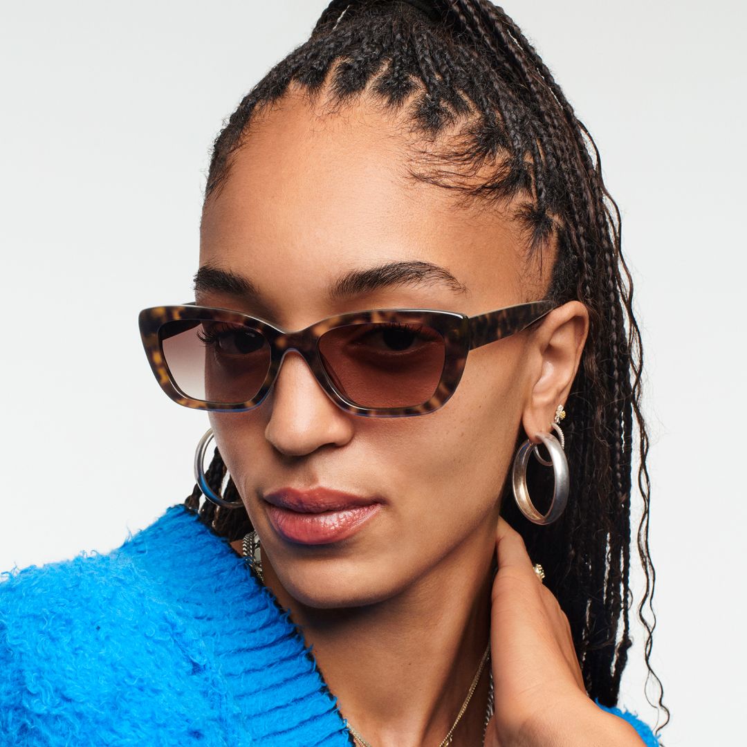 Woman with sunglasses looking at the camera with the hand on the neck.
