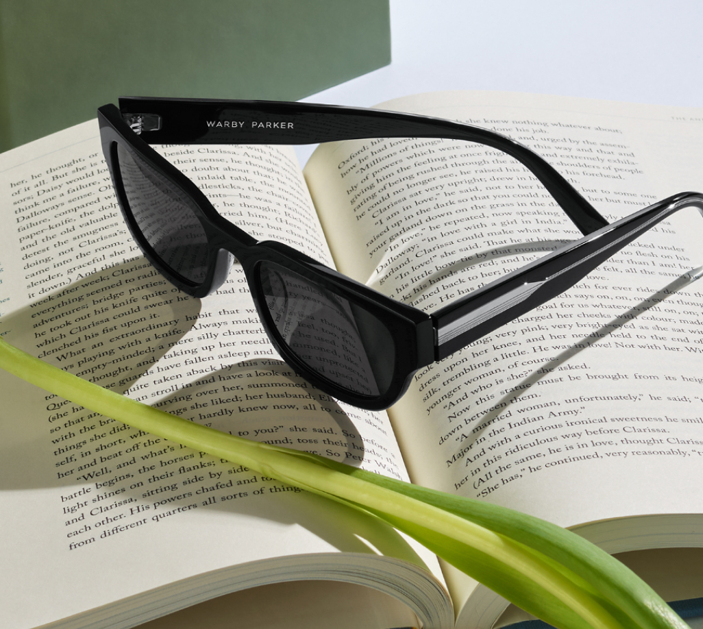 Black sunglasses placed on an open book, with green leaves in the foreground.