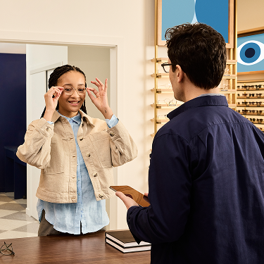 Girl trying on glasses with a staff member at an eyewear store.