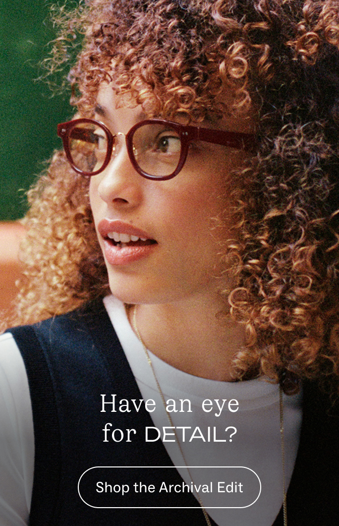 A woman with curly brown hair and glasses looks to the side.