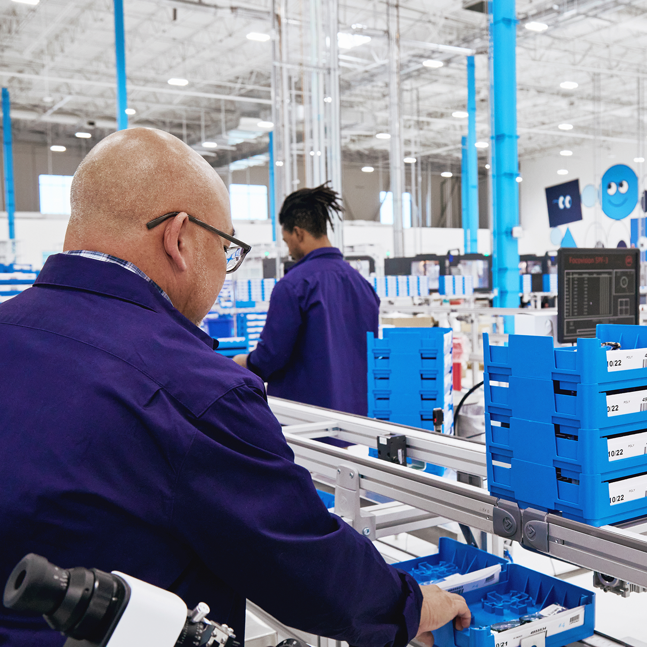 Workers in blue uniforms work on an assembly line in a brightly lit factory.