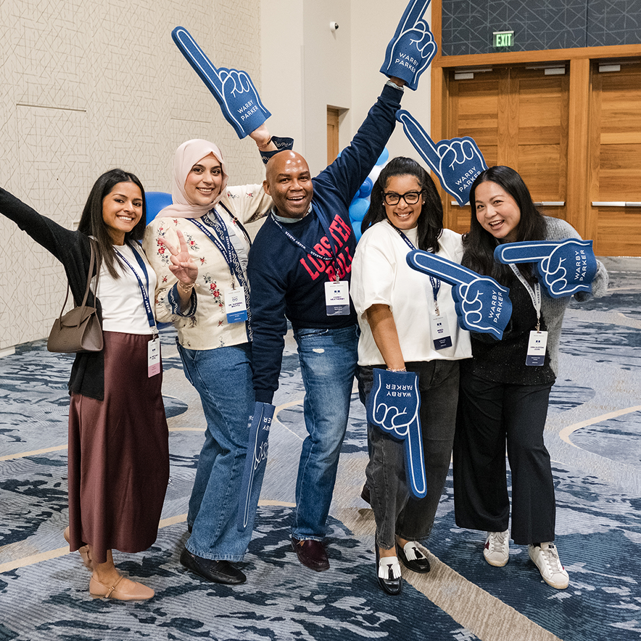 A group of five people are posing for a photo with foam fingers, all smiling and having a good time.