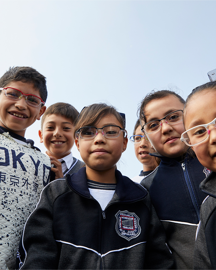 Children in school uniforms and glasses smiling at the camera outdoors with a clear sky background.