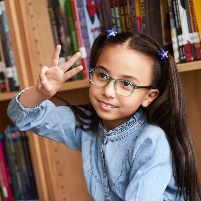 Smiling girl with glasses in front of a bookshelf.
