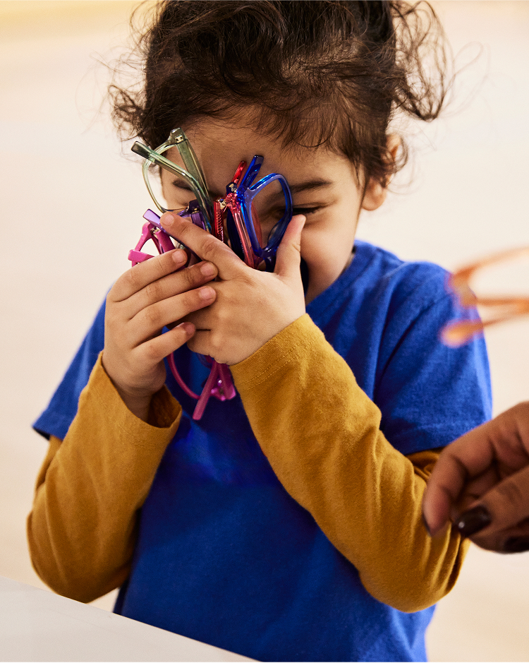 A smiling girl grabbing many glasses close to her face.