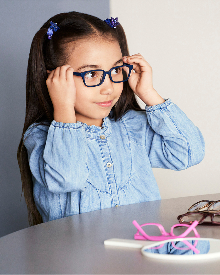 A smiling girl wearing glasses, holding the glasses with her hands.
